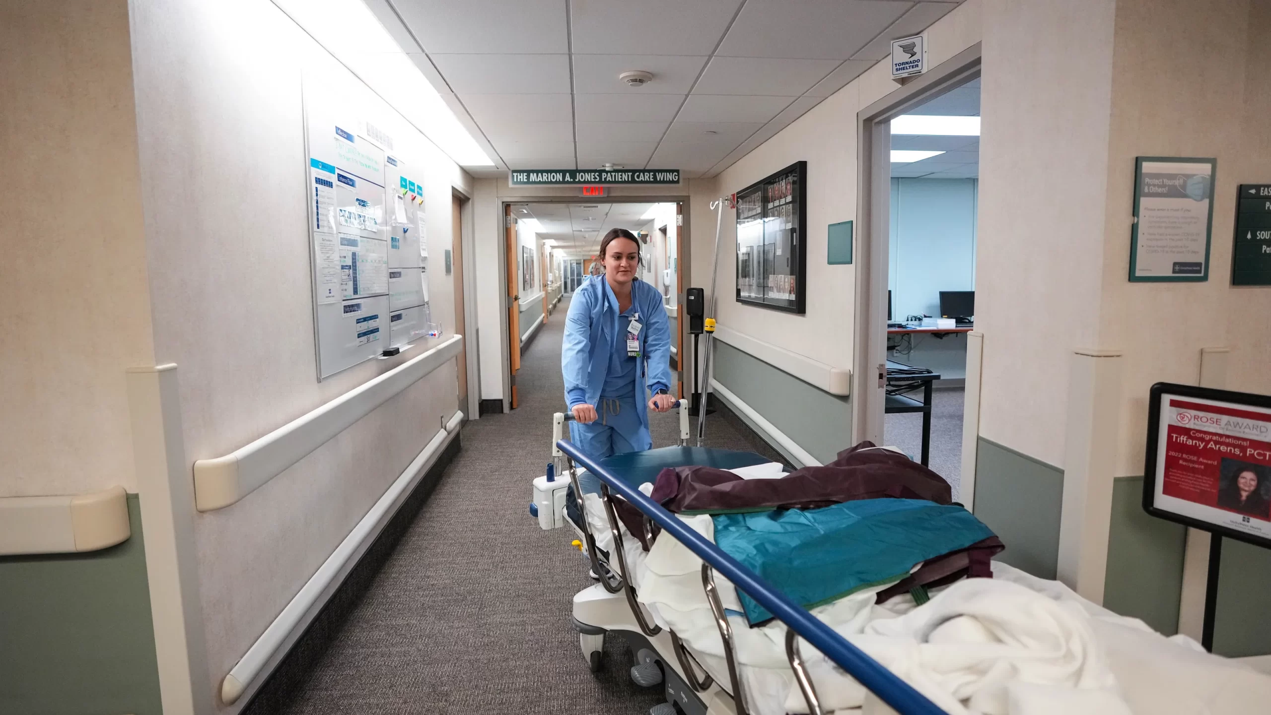 A scene in a hospital corridor, a staff person pushes a gurney around a corner. 