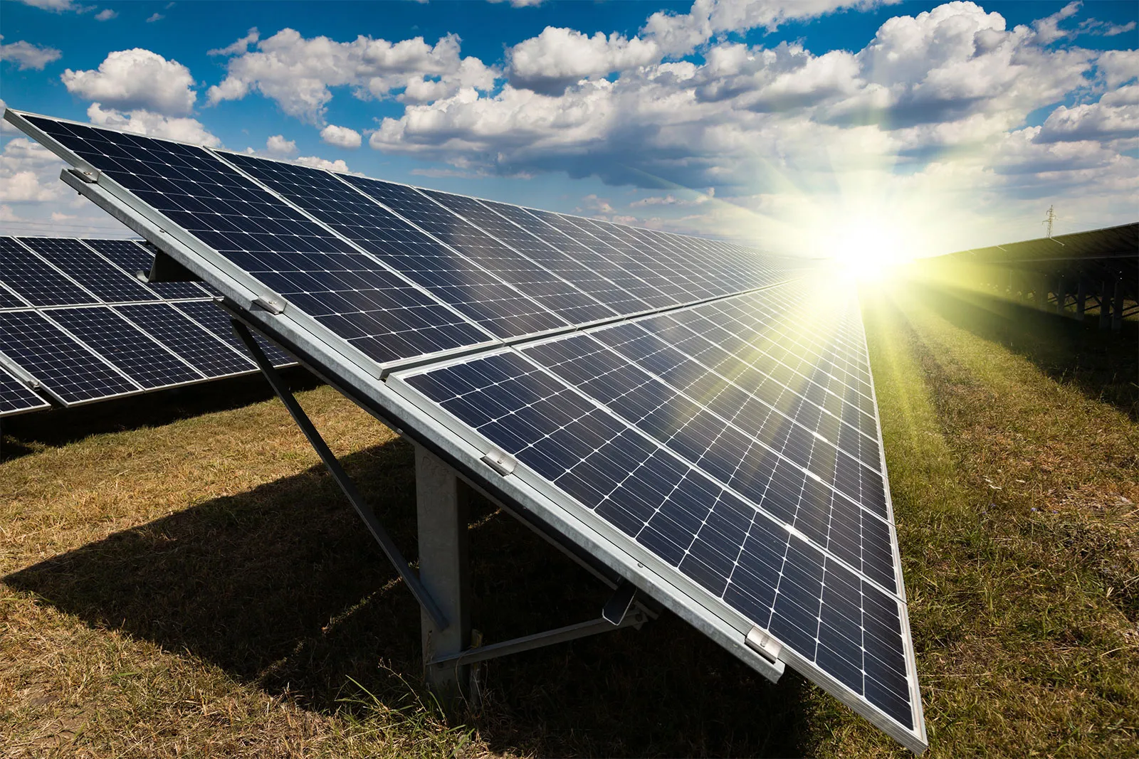A row of solar panels in bright sunlight; the sky is blue with puffy whites clouds. 